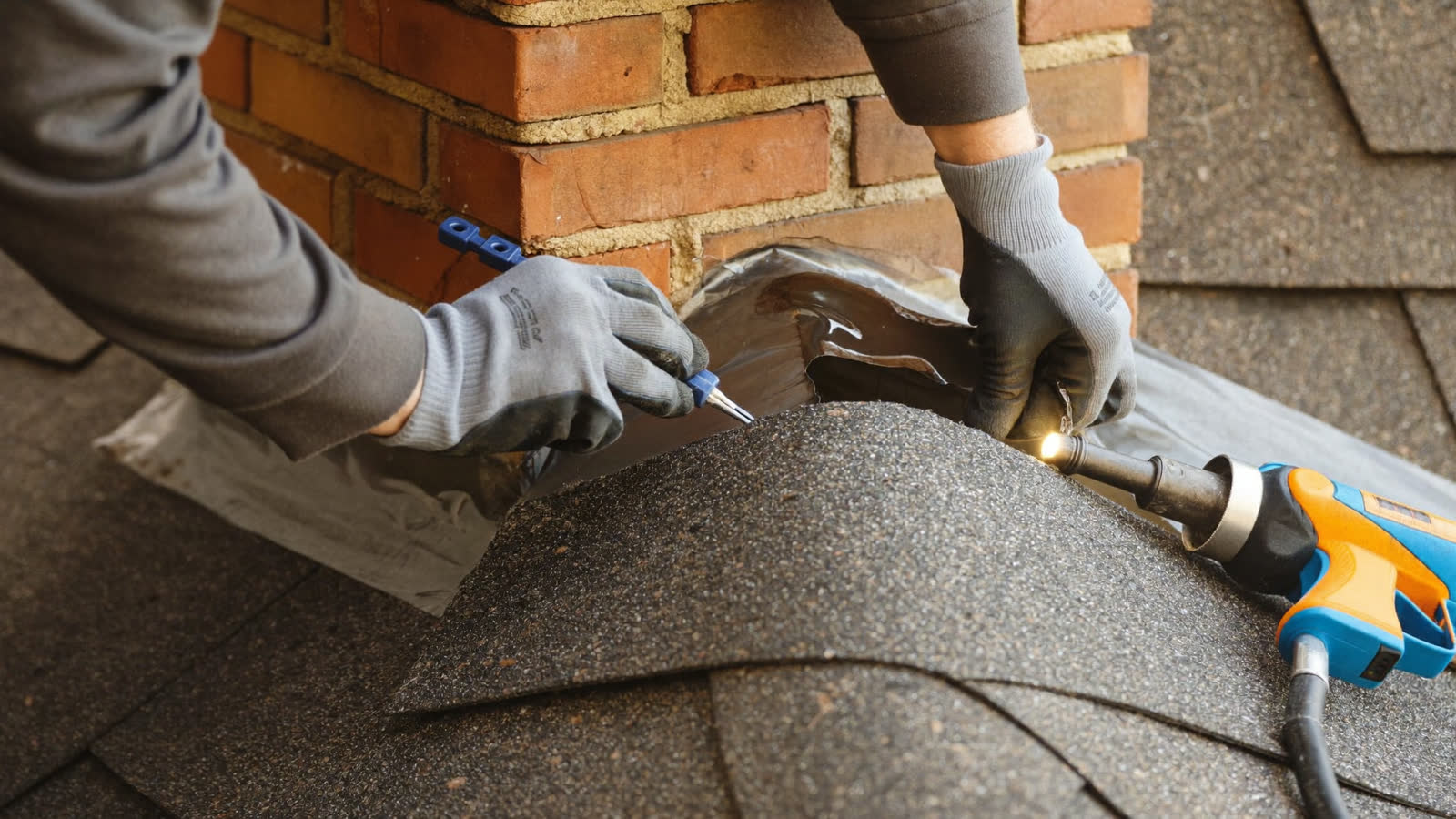Roofer repairing step flashing along a chimney